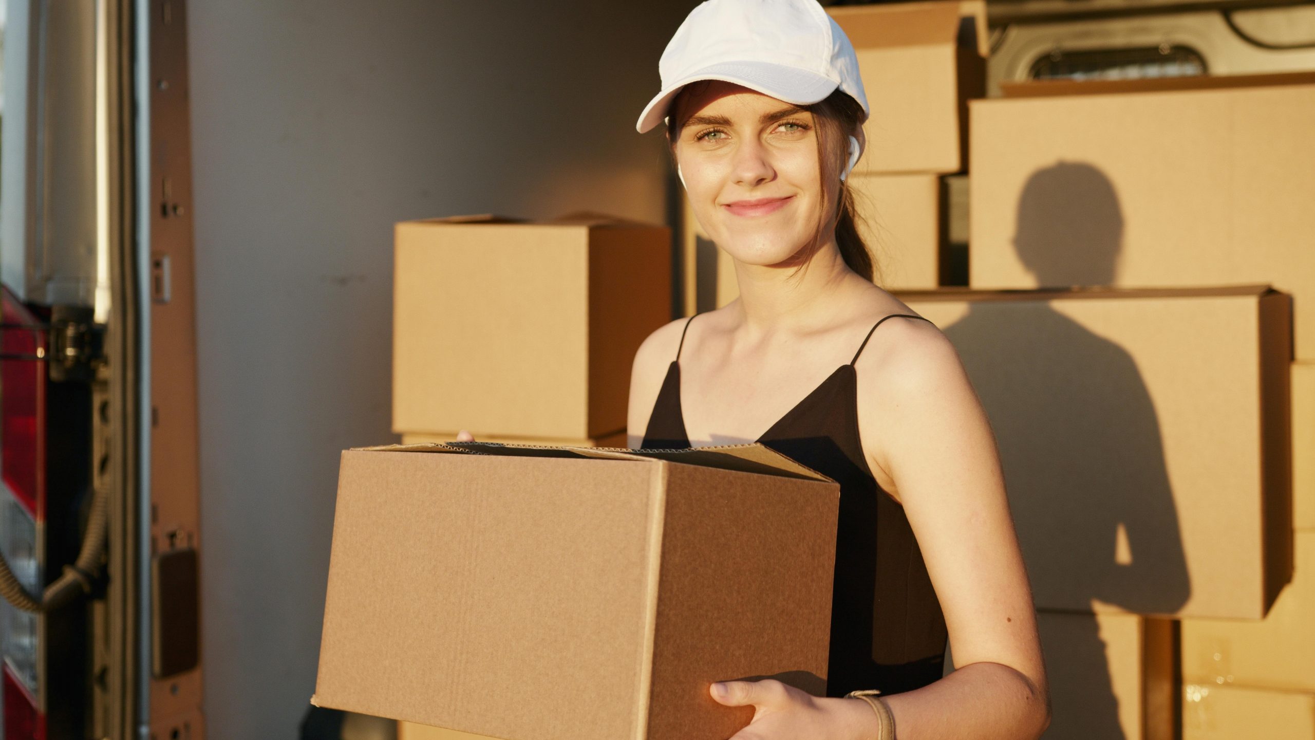 woman in a white cap carrying a moving box out of a van