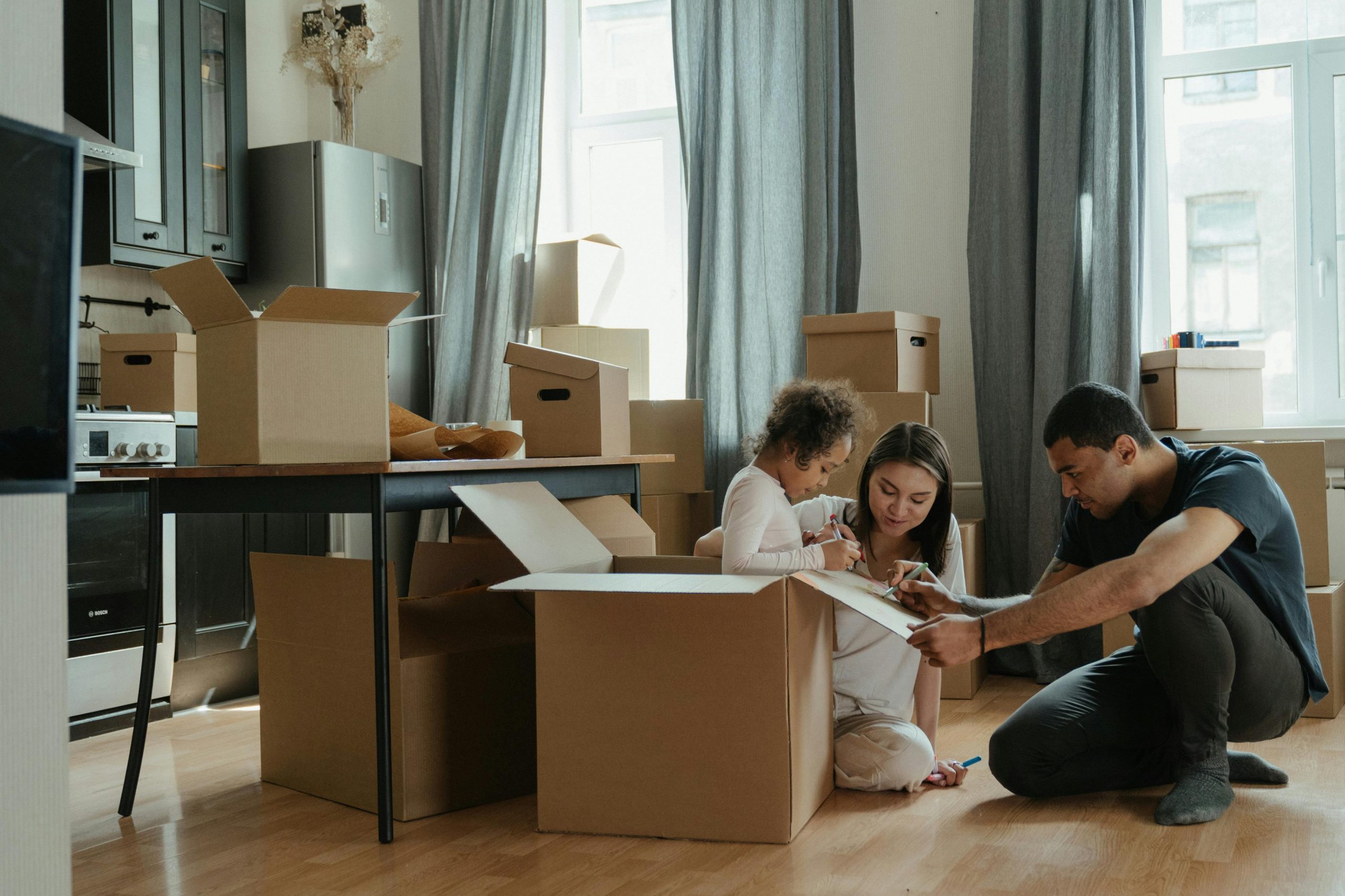 family who just moved into a new house, with a toddler standing inside a moving box