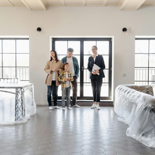realtor guiding a family into their new home, with furniture covered in plastic