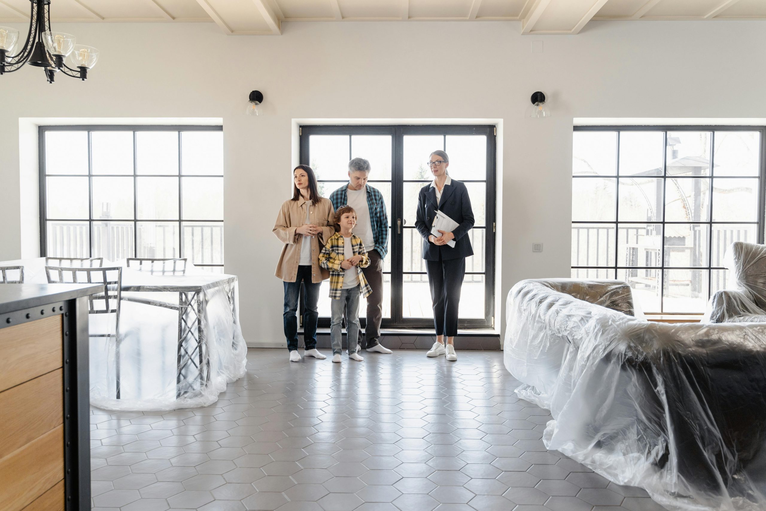 realtor guiding a family into their new home, with furniture covered in plastic