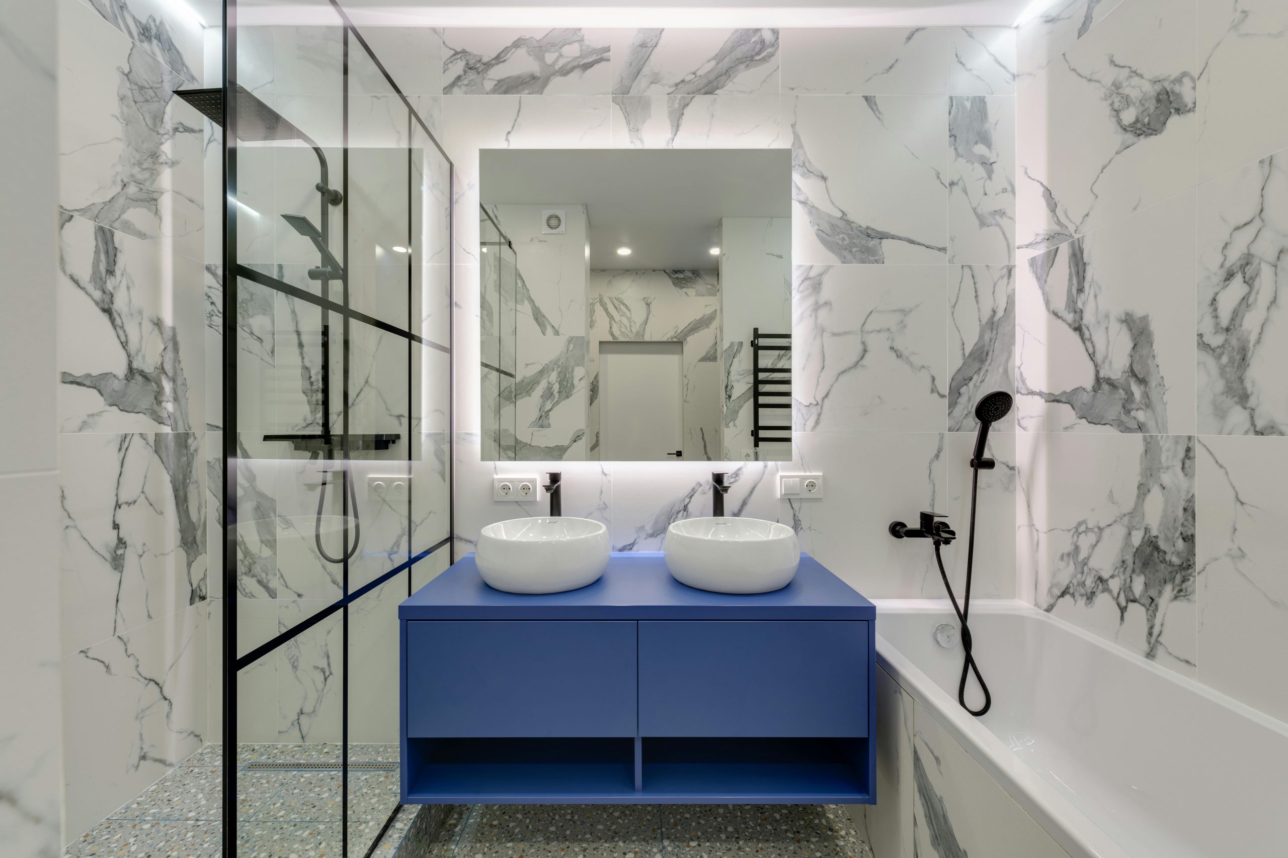 marble bathroom with a blue double-sink vanity and bathtub