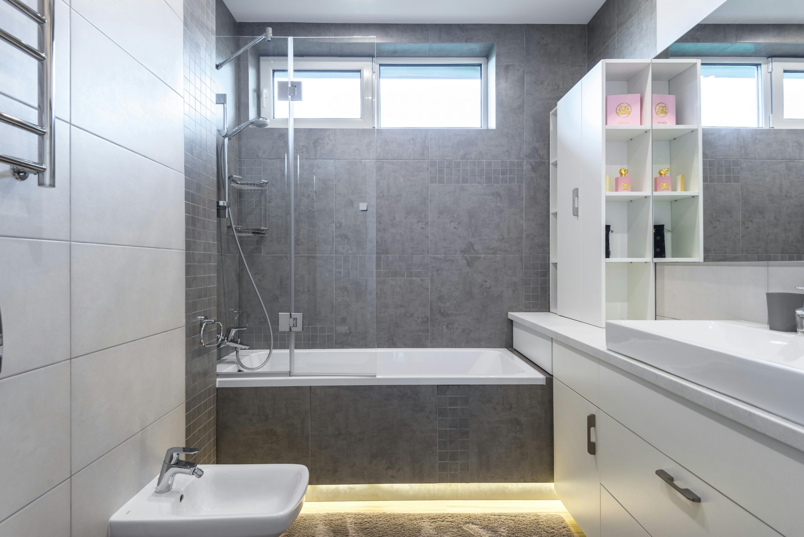 small bathroom with gray tiles and lighting beneath a bathtub
